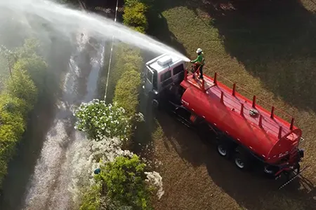 Caminhão pipa realizando a irrigação de gramado em área externa.