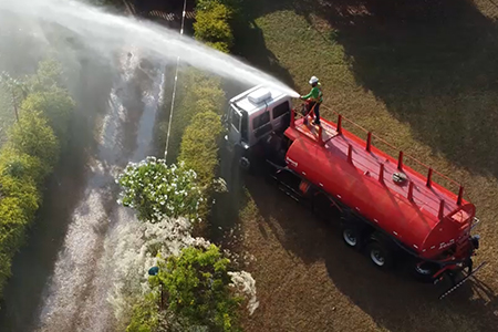 Caminhão pipa realizando a irrigação de gramado em área externa.
